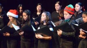 A group of childern singing, holding sheet music.